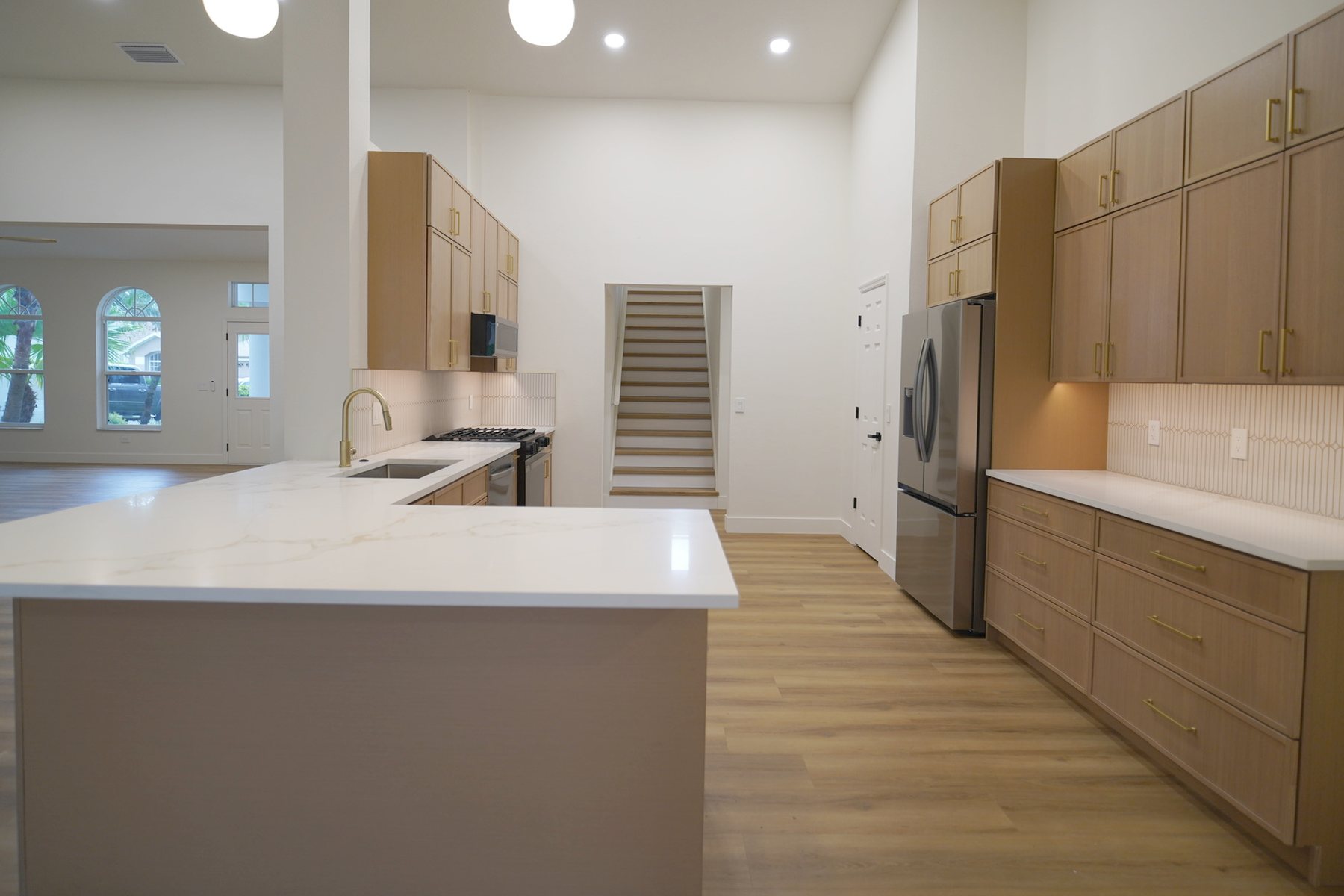 The same kitchen finished: light oak cabinetry, a quartz-topped island, and wood flooring running through to the entry.