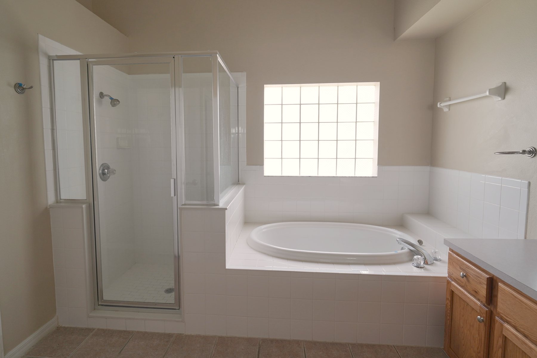 Primary bathroom before the remodel: a framed glass shower enclosure, a built-in garden tub under a glass-block window, and an oak vanity.