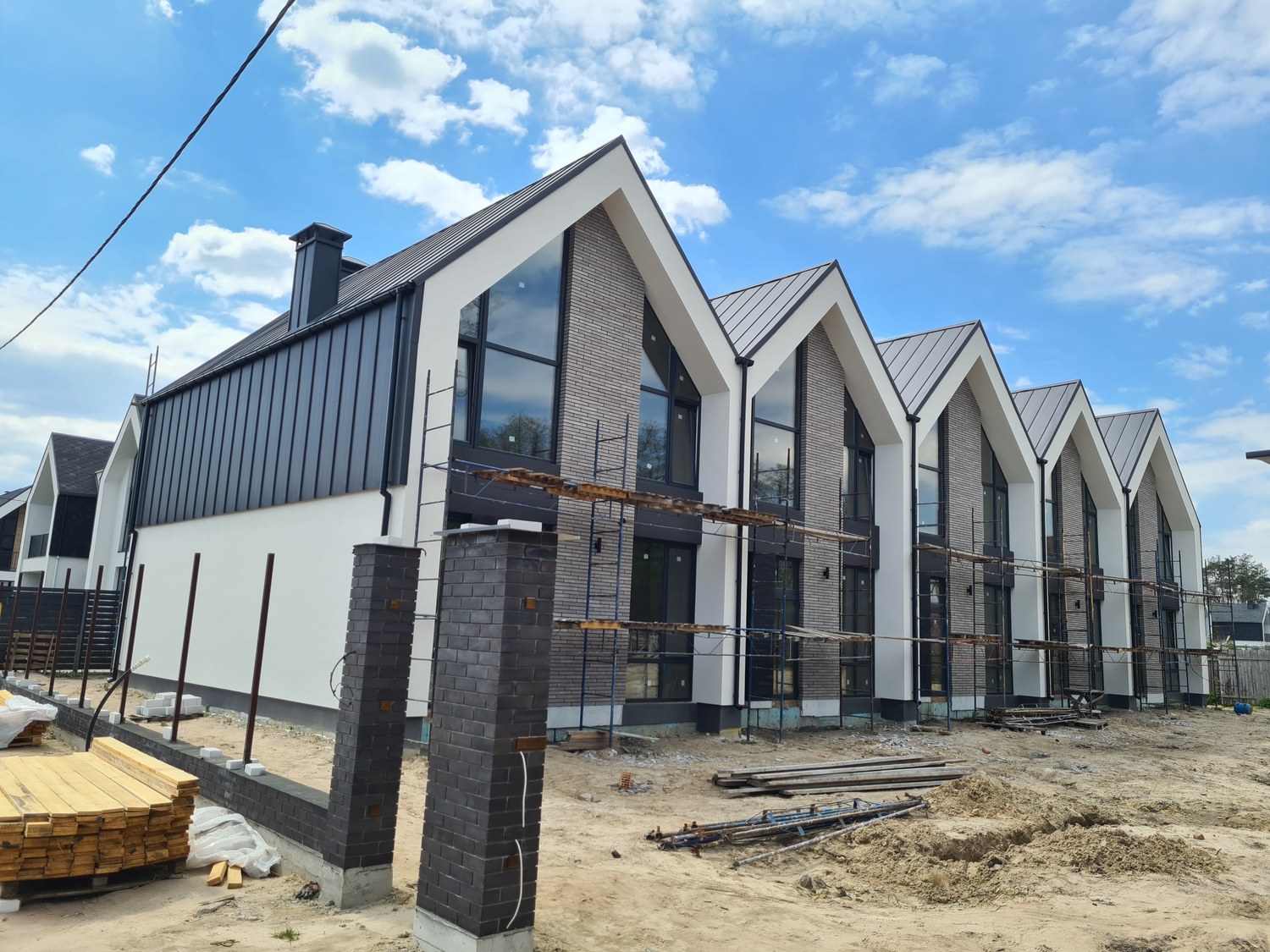 Row of townhouses with standing-seam roofing and brick facade complete, scaffolding still up during envelope construction.