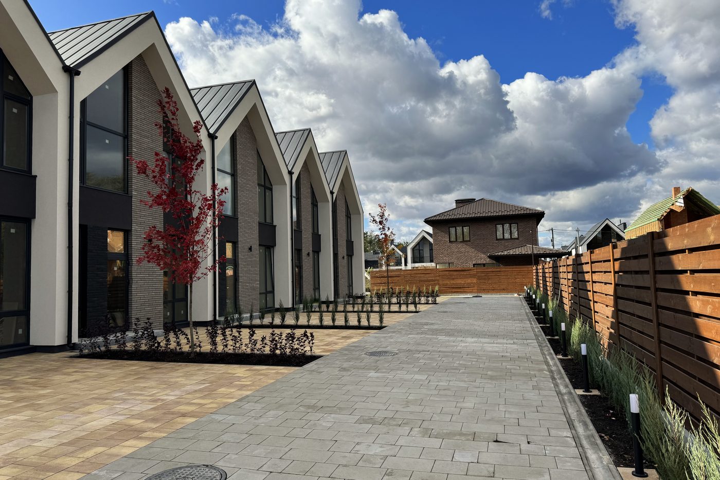 The finished terrace along a paved path, with planting and a red-leaved tree.