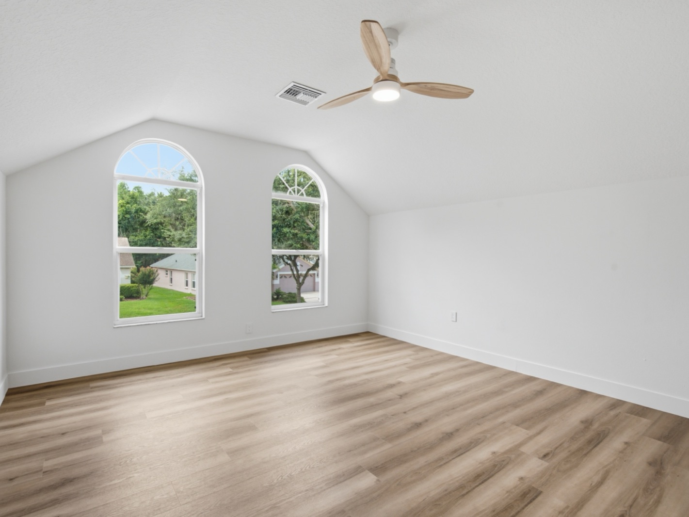 Renovated bedroom with vaulted ceiling, arched double windows, and a wood ceiling fan.