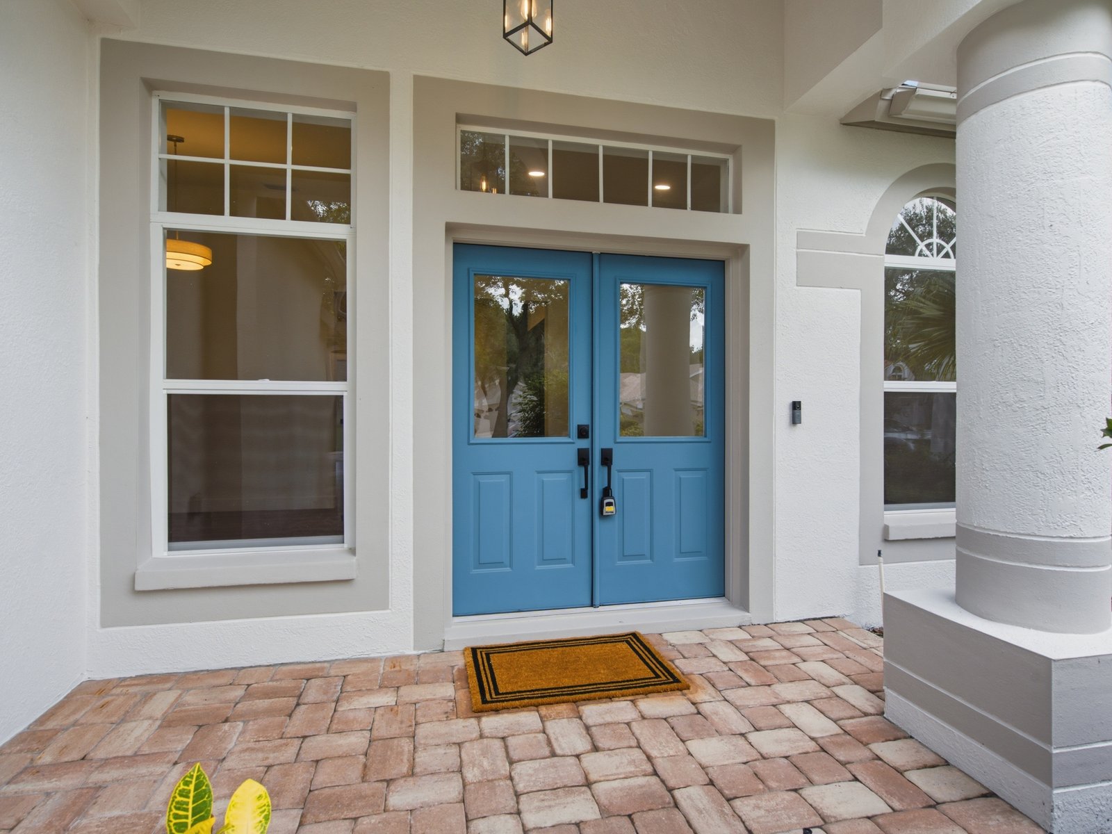 Renovated entry with blue double doors, brick pavers, and columns.