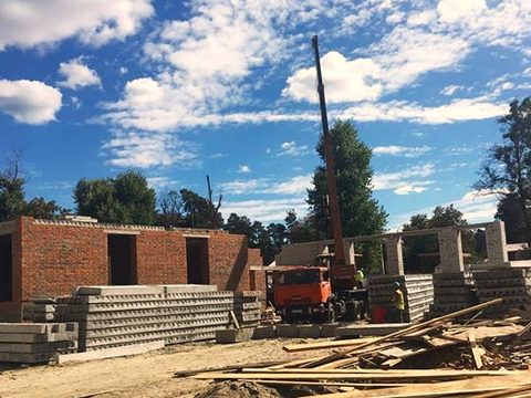 Load-bearing brick walls at ground level, precast hollow-core floor slabs stacked beside them and a truck crane behind.