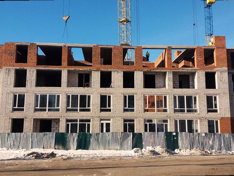 The building at its fourth floor: pale brick below, red brick on the top course, tower cranes overhead.