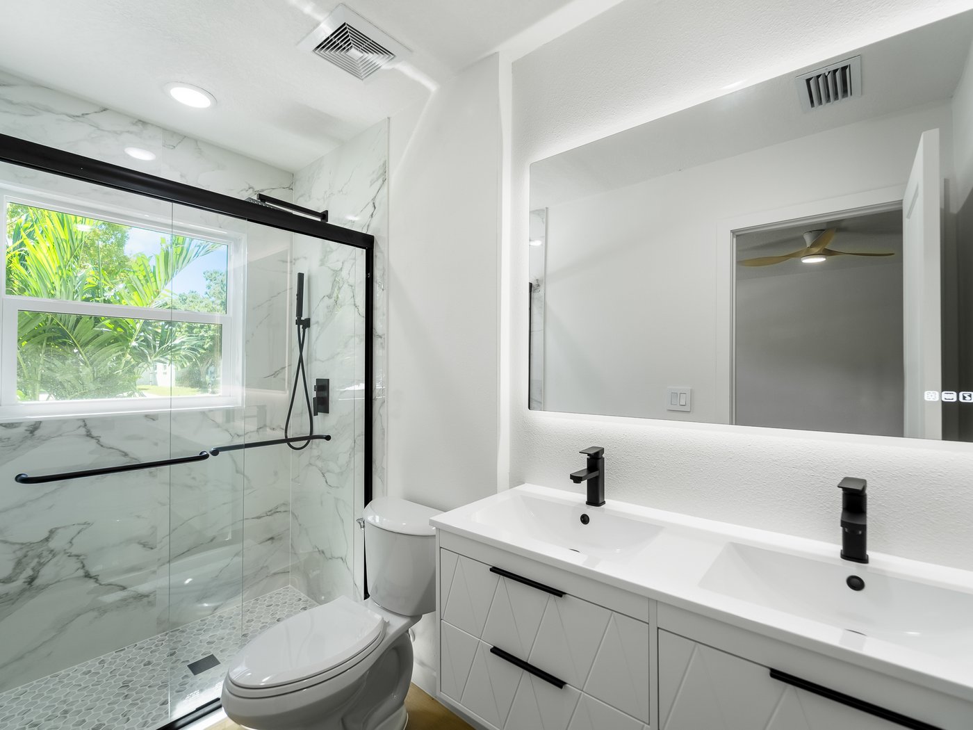Finished bathroom with a marble-tiled glass shower, black fixtures, and a backlit mirror.