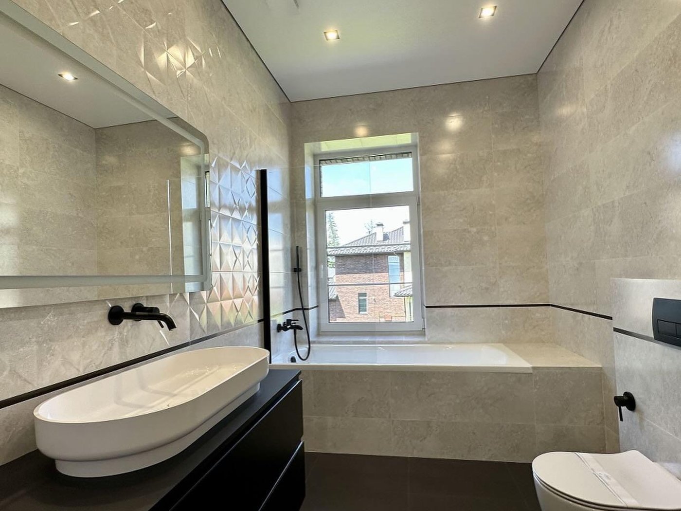 Finished bathroom in light travertine tile, with a built-in tub and black wall-mount fixtures.