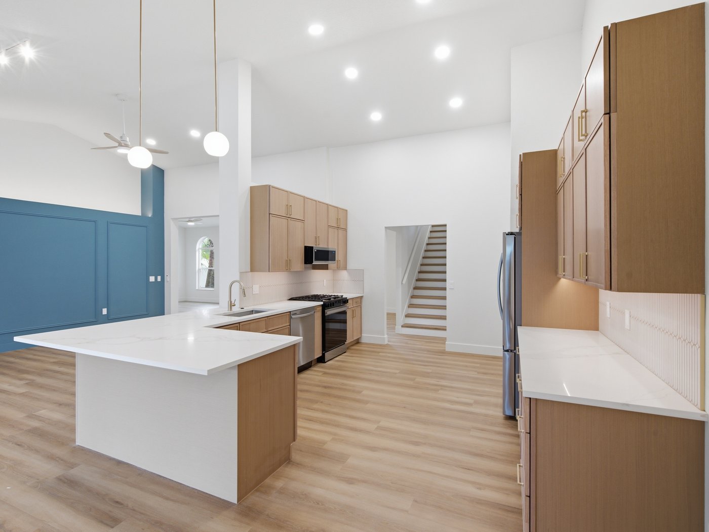 Renovated kitchen with pendant lighting, a navy accent wall, and light wood cabinetry under a vaulted ceiling.