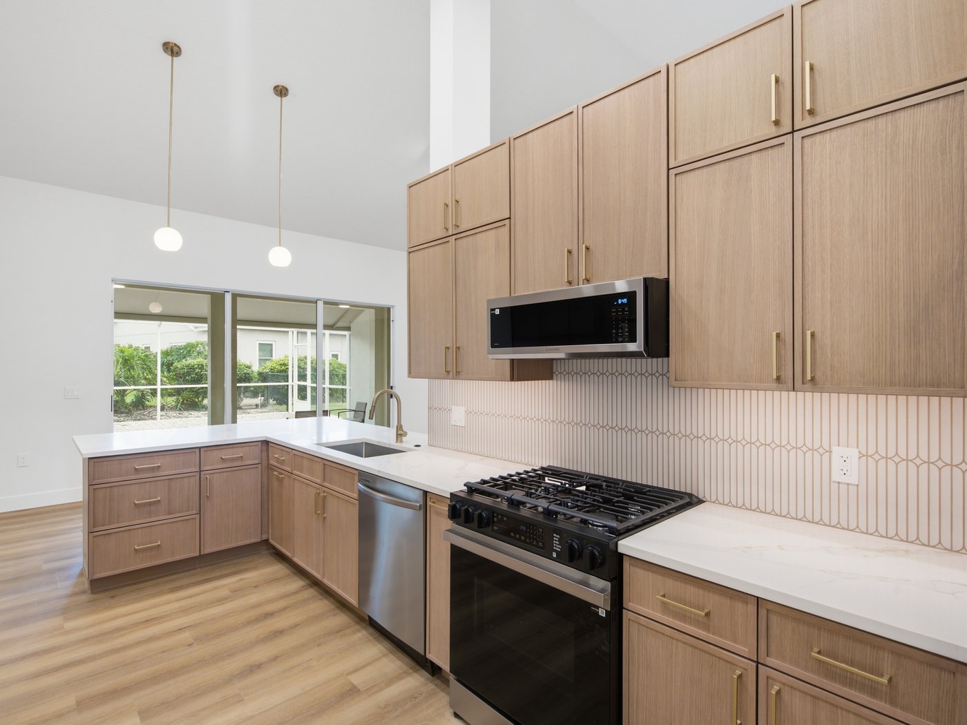 Finished kitchen cooking nook with light wood cabinetry, gas range, and a window view of greenery.