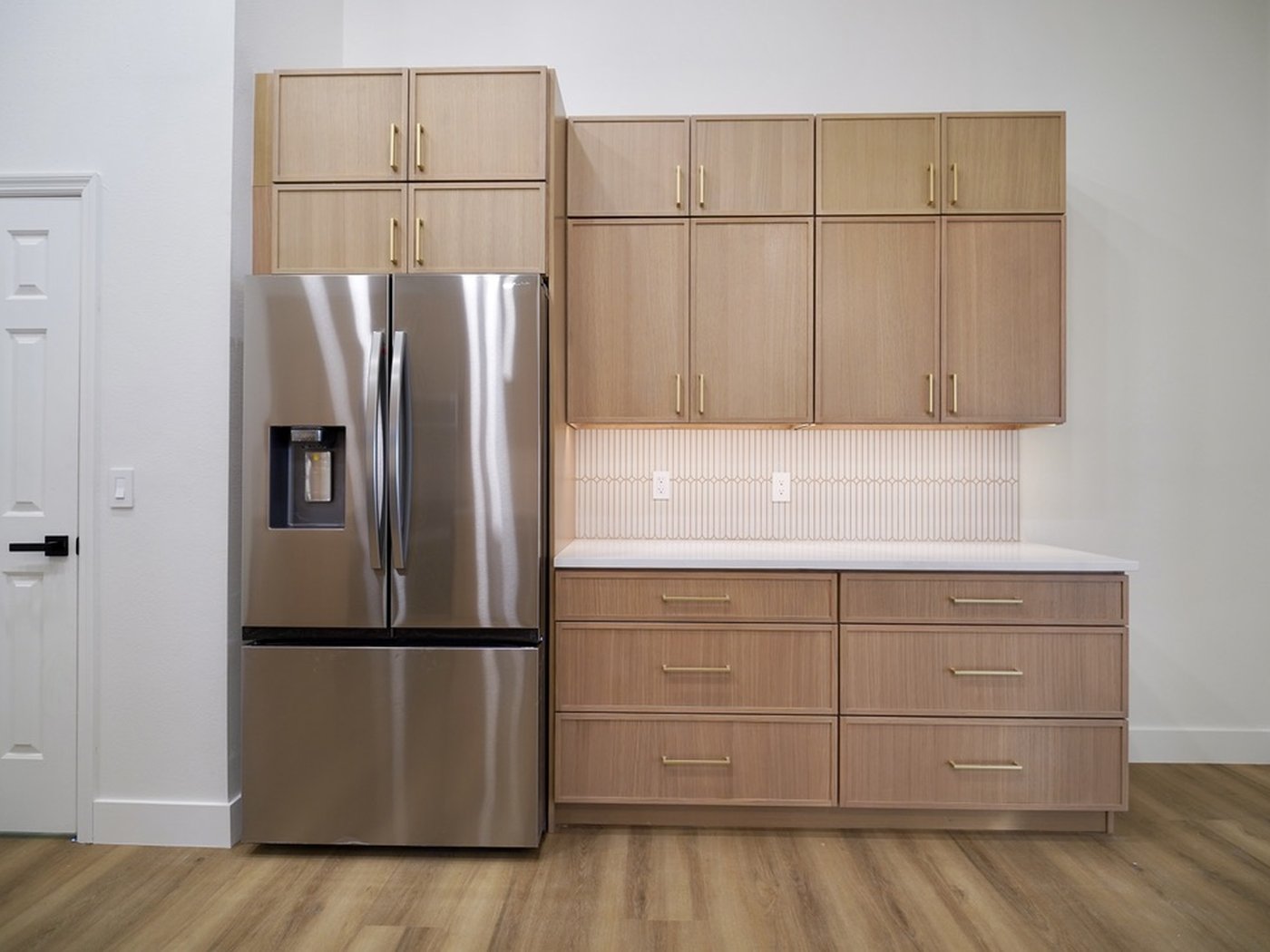 Finished kitchen with a stainless refrigerator and light wood cabinetry, hardware detail.