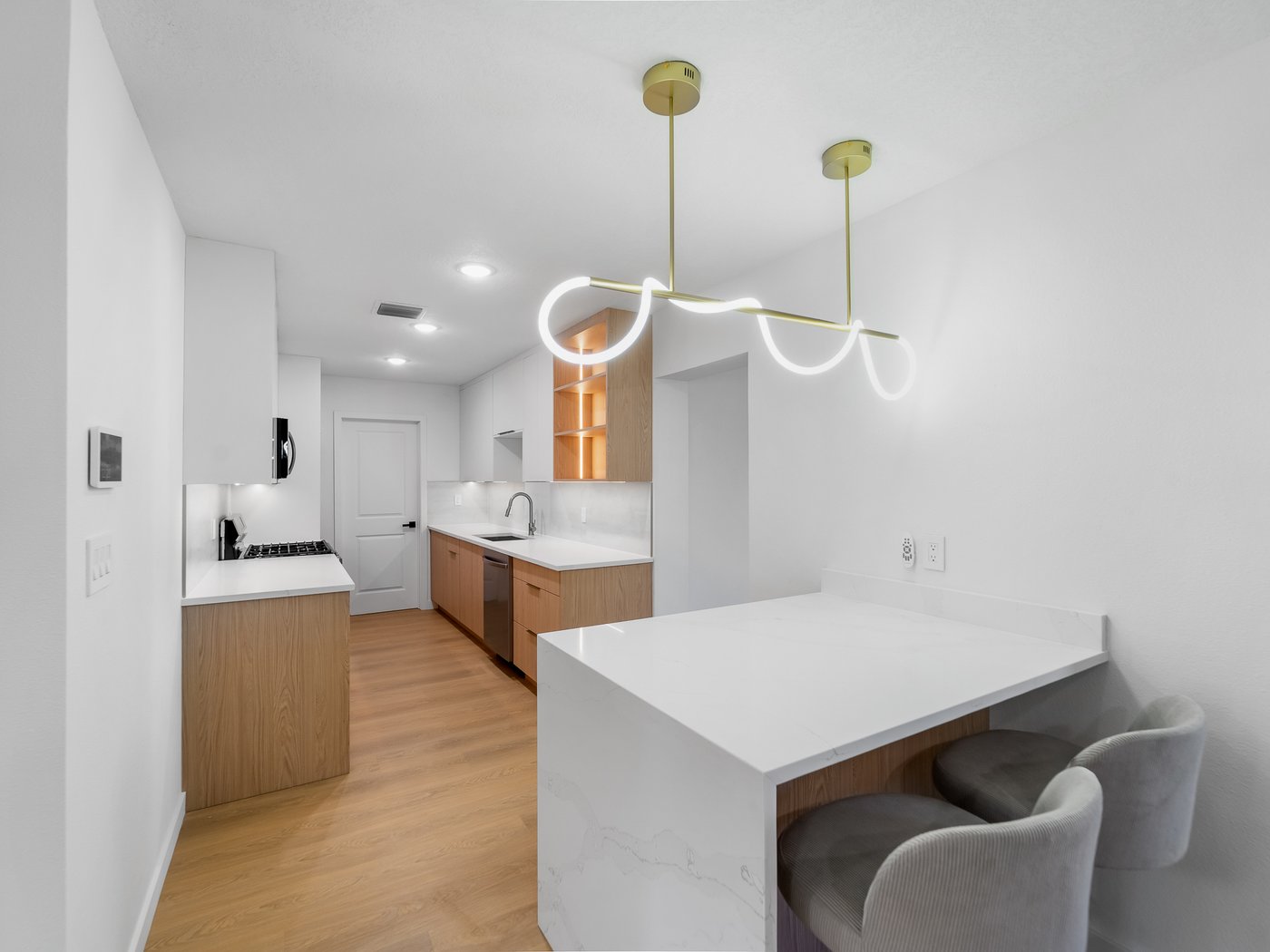Finished kitchen with a sculptural wavy light fixture, light wood cabinetry, marble waterfall island, and banquette seating.