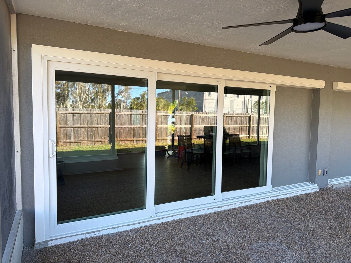 Finished three-panel sliding glass door opening onto a screened lanai, with a wood fence and patio seating visible beyond.