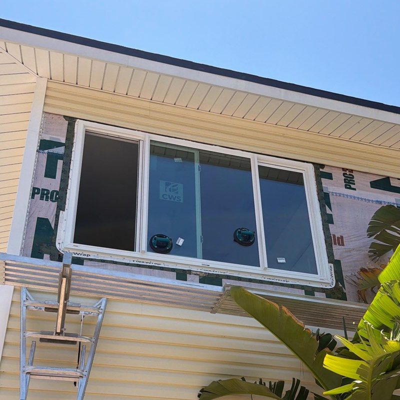 The new white impact unit set into the same opening, flashing tape run along the sill and up the jambs over the housewrap, the siding not yet closed.
