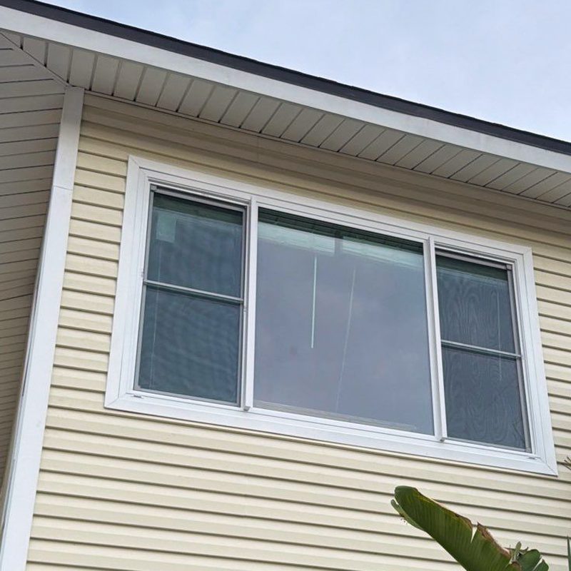 The same opening finished — the new three-panel impact window in place and the cream siding closed around it.