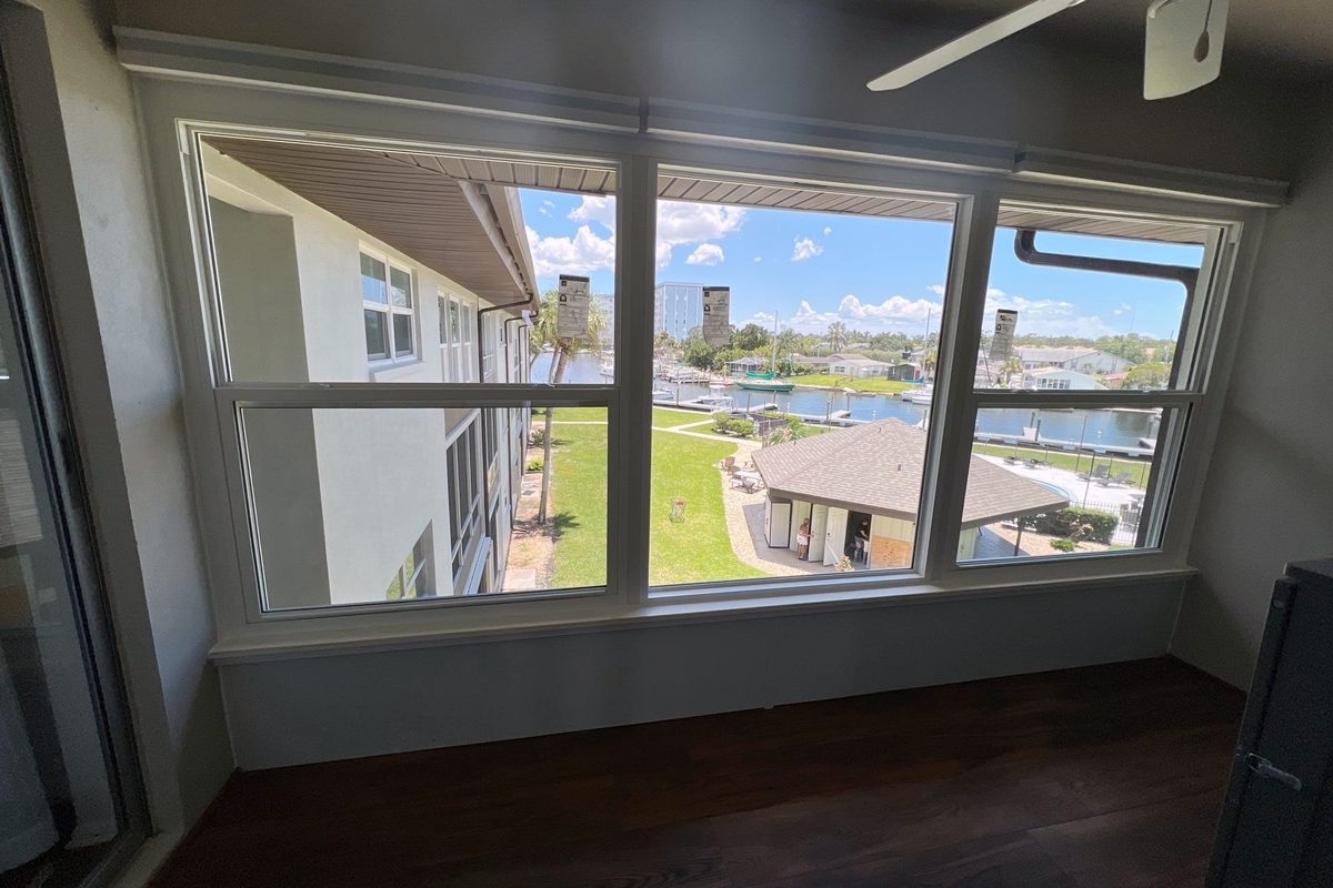 A finished room looking out over a marina through a wide bank of impact windows, dark wood floor below.