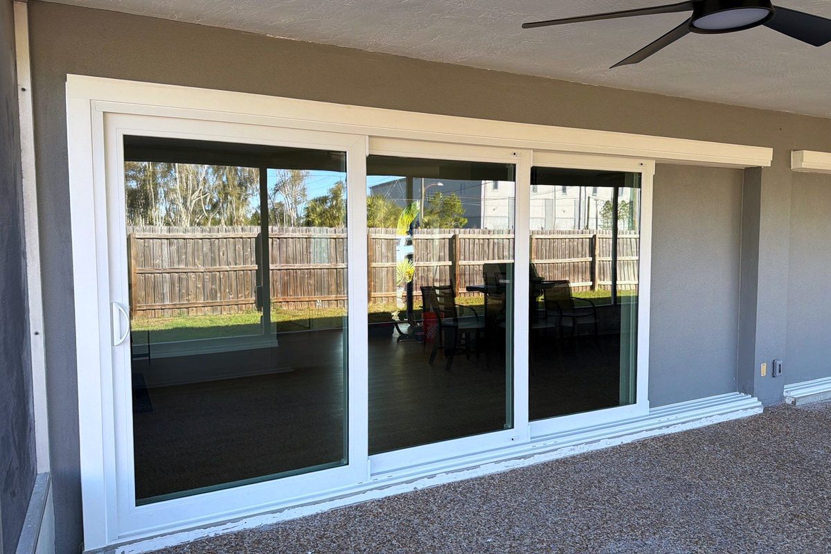 The same four-panel impact slider finished — tape off, sealant run, the screened lanai and garden beyond.